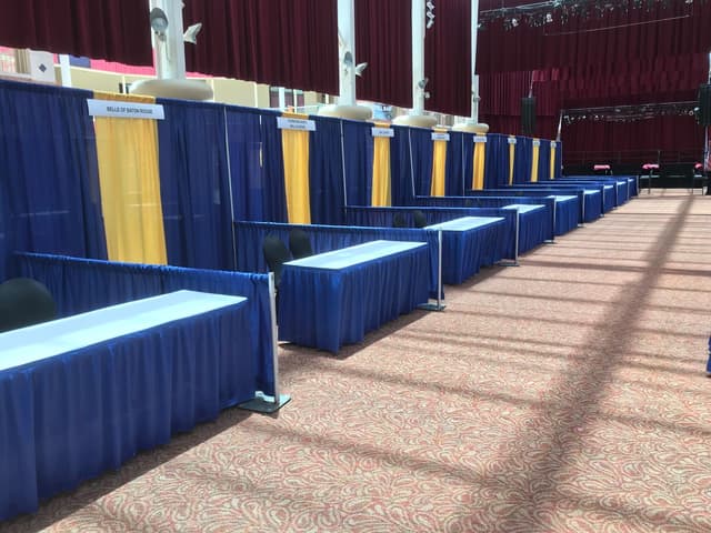 Blue and gold pipe and drape booths with blue-skirted tables in a theater venue
