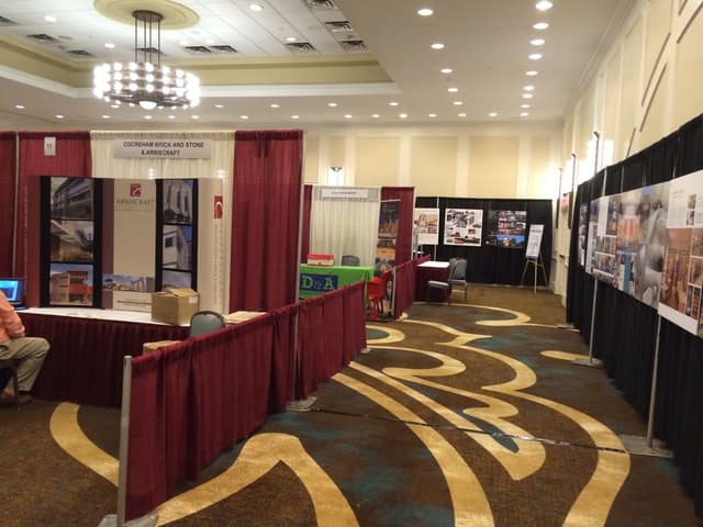 Exhibit hall with maroon and black pipe and drape booths on patterned carpet